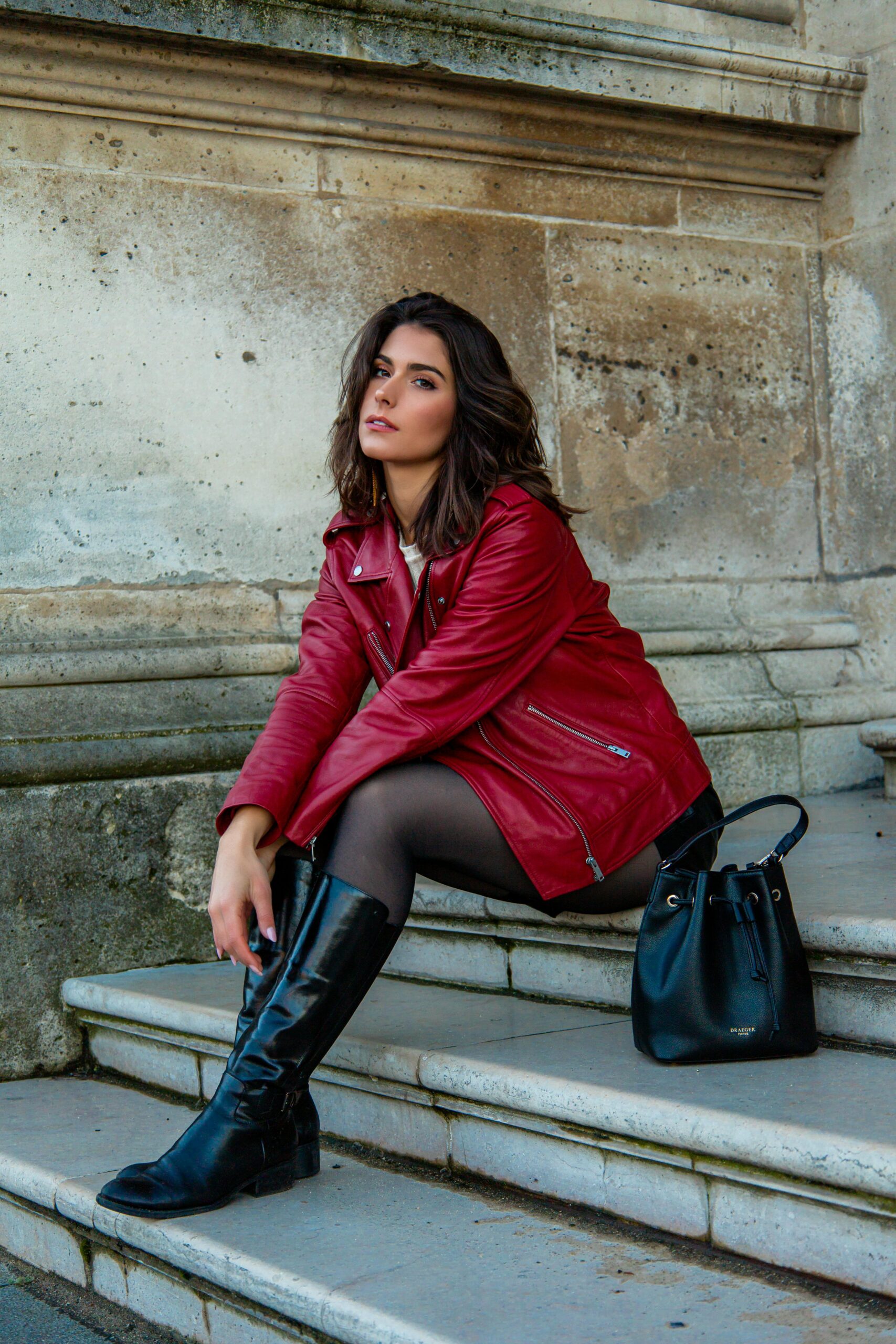 A stylish woman in a red jacket poses on steps with a Parisian background.