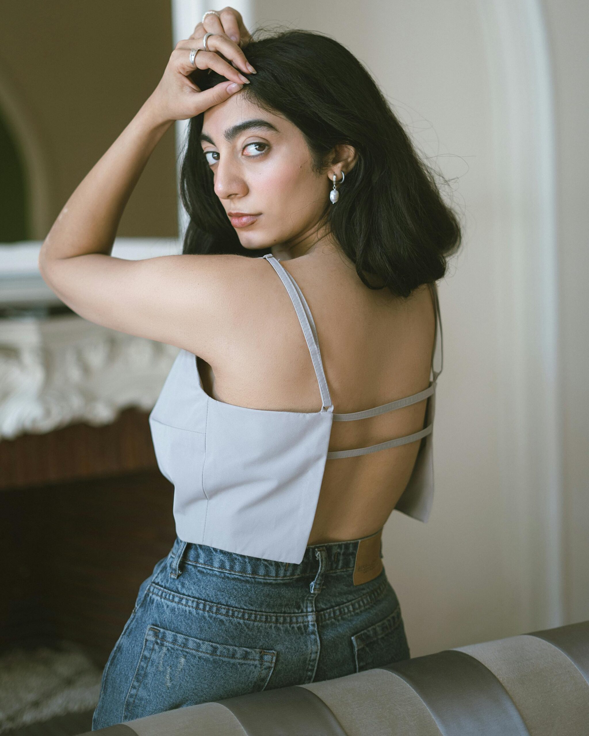 Fashionable woman wearing blue jeans and a backless top in an elegant indoor setting.